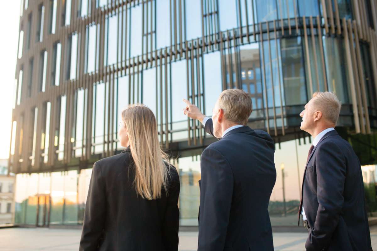 A group of business people looks toward a high-rise building, commercial real estate for sale concept