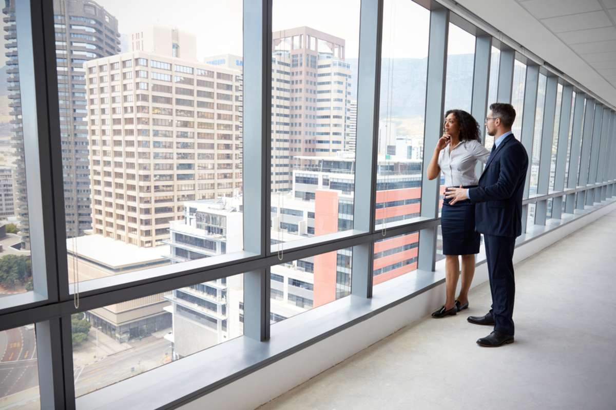 Businessman and woman look out from an empty office space, commercial real estate management concept