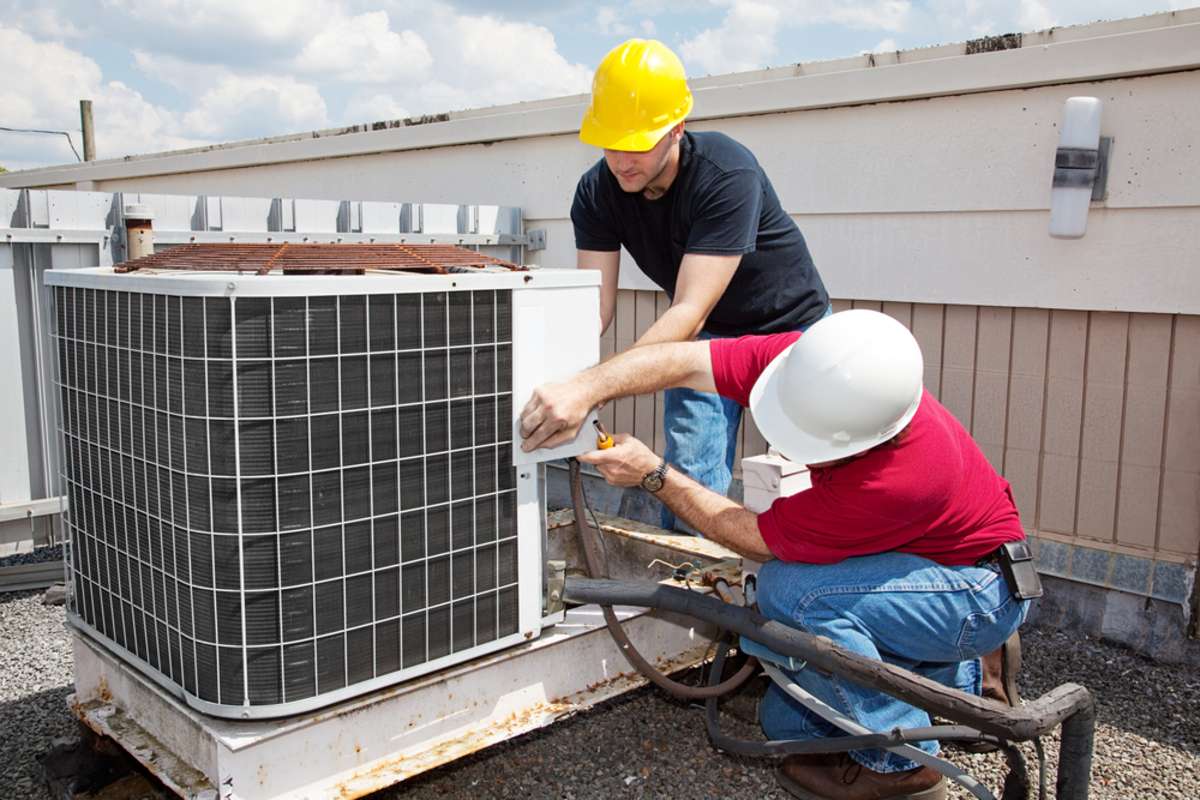 Two workers and a commercial air conditioner on a roof, commercial property management companies concept