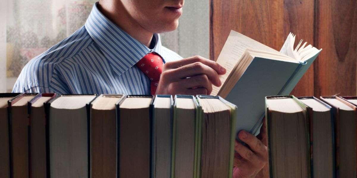 Man reading a book next to the bookshelf