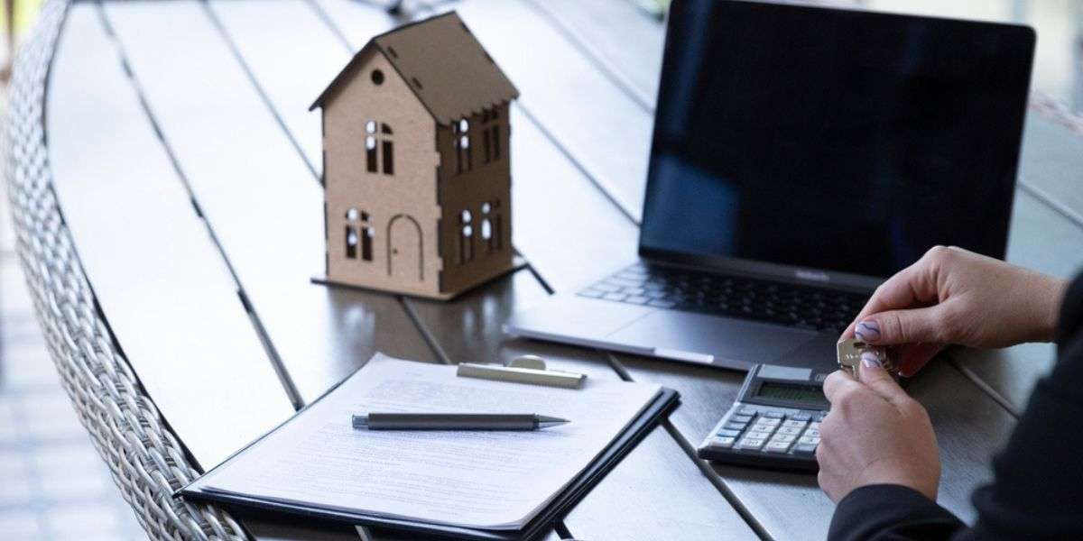 Manager holds apartment key sitting at table with laptop papers and toy house