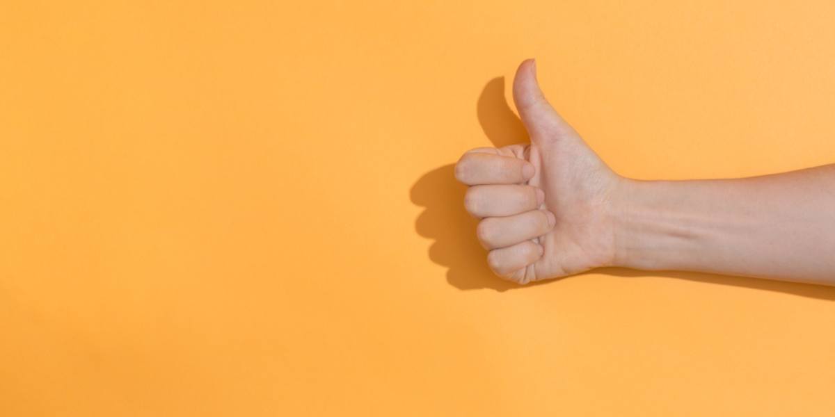 Person doing thumbs up gesture on a orange background